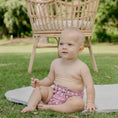 Load image into Gallery viewer, Baby wearing a Reusable Cloth Nappy – Monstera Pink | 2.0 | My Little Gumnut shown outdoors for a lifestyle fit image.