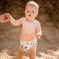 Load image into Gallery viewer, Baby in a Banksia reusable swim nappy playing at the beach, designed for comfort and reducing waste.
