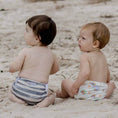 Load image into Gallery viewer, Two toddlers on the beach, both wearing a reusable swim nappy, one in Slate Stripe and the other in a rainbow design.