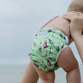 Load image into Gallery viewer, Reusable Swim Nappy featuring colorful cockatoo prints on a baby at the beach.