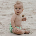 Load image into Gallery viewer, A baby wearing a Cockatoo reusable swim nappy, playing on the beach sand, perfect for water activities.