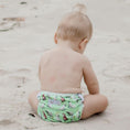 Load image into Gallery viewer, Baby wearing a Cockatoo reusable swim nappy sitting on the beach, ideal for water play and reducing waste.