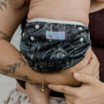 Load image into Gallery viewer, Reusable Swim Nappy - Black Flora on a baby, securely held by an adult, showcasing floral design and comfort.