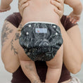 Load image into Gallery viewer, Baby wearing a Black Flora reusable swim nappy by My Little Gumnut, perfect for beach and pool play.
