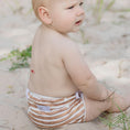 Load image into Gallery viewer, Baby sitting on the sand wearing a Reusable Swim Nappy in brown stripes, perfect for beach days and pool play.