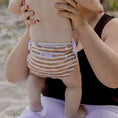 Load image into Gallery viewer, Baby wearing a Reusable Swim Nappy Brown Stripe while being held by a parent at the beach.