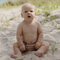 Load image into Gallery viewer, Baby sitting on the sand wearing a Reusable Swim Nappy in Brown Stripe, perfect for beach days.
