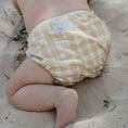 Load image into Gallery viewer, Reusable Swim Nappy in Gingham (Beige) pattern on a baby enjoying a sandy beach day.