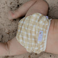 Load image into Gallery viewer, Reusable Swim Nappy in Gingham (Beige) design on a baby at the beach, perfect for comfort and waste reduction.