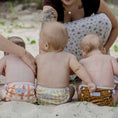 Load image into Gallery viewer, Three babies (all wearing a reusable swim nappy) relaxing on the beach, showcasing the Gingham (Beige) design.