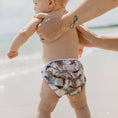 Load image into Gallery viewer, Baby wearing a Reusable Swim Nappy at the beach, enjoying fun in the sun with family.