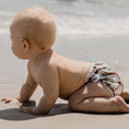 Load image into Gallery viewer, Baby crawling in a Reusable Swim Nappy on the beach, showcasing the Kookaburras design from My Little Gumnut.