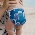 Load image into Gallery viewer, Reusable Swim Nappy - Rainbow (Blue) on a baby, ideal for beach and pool days, designed for comfort and waste reduction.