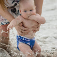 Load image into Gallery viewer, Baby enjoying the beach in a Reusable Swim Nappy - Rainbow (Blue) while splashing in the water.