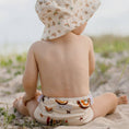 Load image into Gallery viewer, Child sitting on the beach wearing a Reusable Swim Nappy - Rainbow (Earth Tones) from My Little Gumnut.