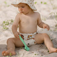 Load image into Gallery viewer, Child playing in sand wearing a Reusable Swim Nappy - Rainbow (Earth Tones) and a sun hat.
