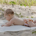 Load image into Gallery viewer, Baby lying on a towel wearing a Reusable Swim Nappy, perfect for beach days with comfort and style.