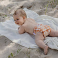 Load image into Gallery viewer, Baby on a sandy beach wearing a Reusable Swim Nappy - Gingham (Rust), enjoying sunny outdoor fun.