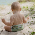 Load image into Gallery viewer, Baby sitting on sand wearing a Reusable Swim Nappy - Sage, enjoying a day at the beach.