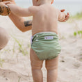Load image into Gallery viewer, Baby wearing a Reusable Swim Nappy - Sage at the beach, promoting comfort and ease for swim adventures.