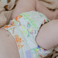 Load image into Gallery viewer, Baby wearing a Reusable Cloth Nappy – Tropical Garden | 2.0 | My Little Gumnut shown lying down to demonstrate flexibility and fit.