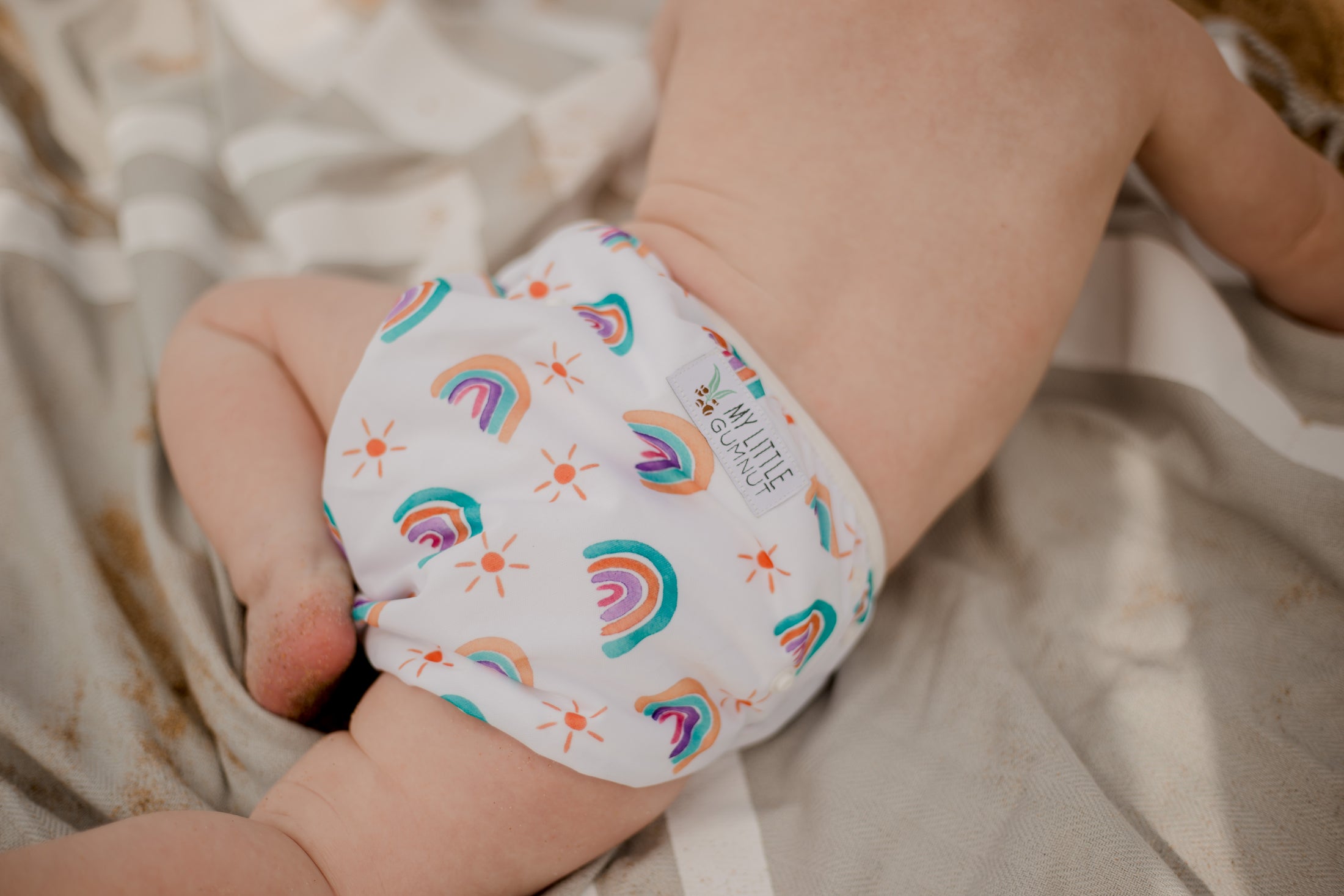 beach baby wearing  pastel rainbow swimming nappy. Australian artist designed swim nappy. My little Gumnut. 